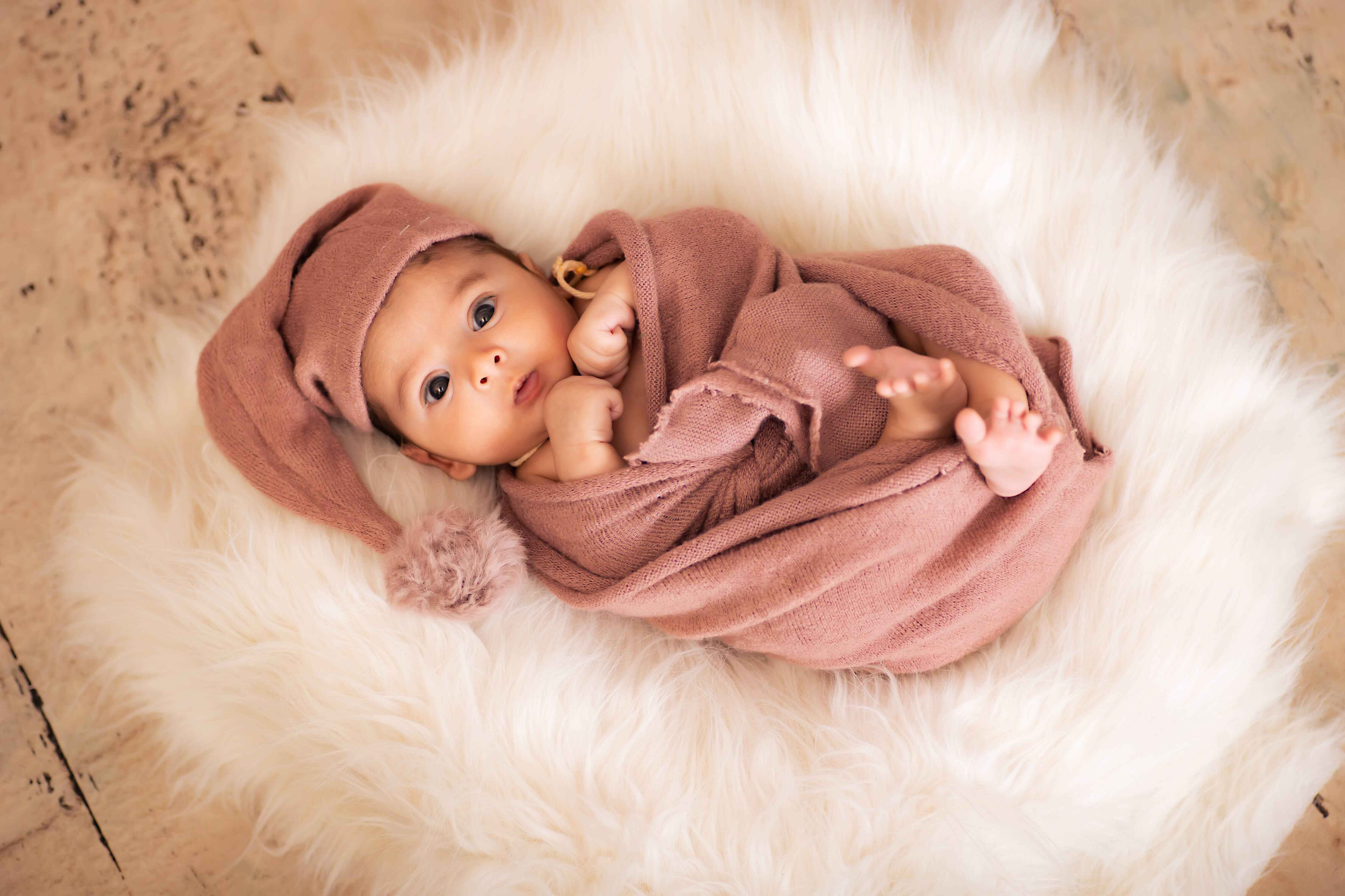 A sweet baby in a brown dress, lying on a cozy fur pillow, for an adorable baby photoshoot.
